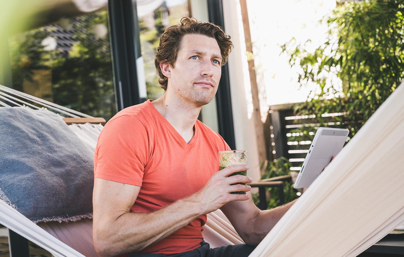 Mann in Hängematte plant Terrassenüberdachung und genießt einen Drink.